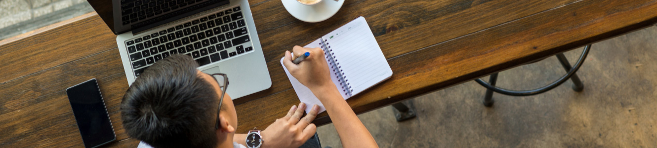 Person writing in a notebook at a table in a cafe