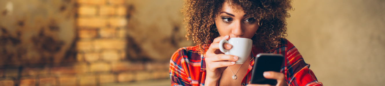 Woman sipping on a cup of coffee while looking at her phone