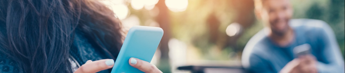 A woman holds her cellphone as she sits on a bench outside on a sunny day. 